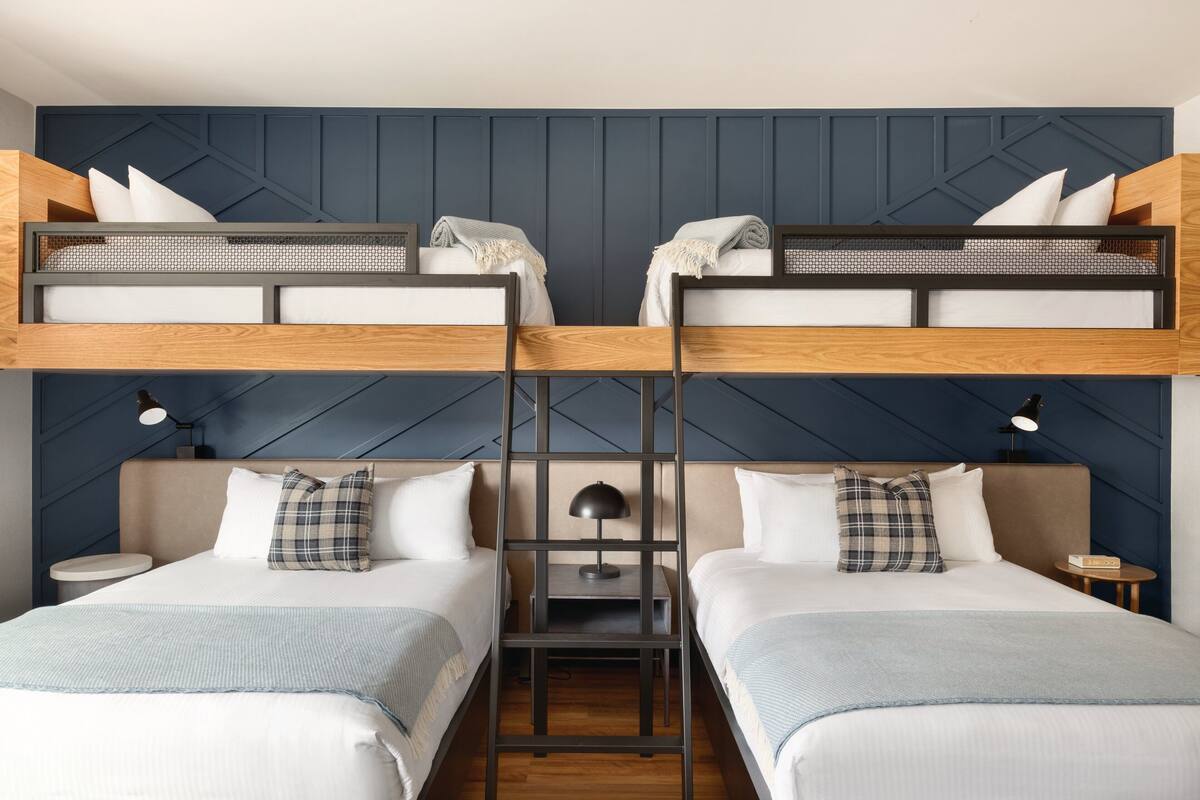 A room with two beds, a ladder, and a desk with a lamp.
