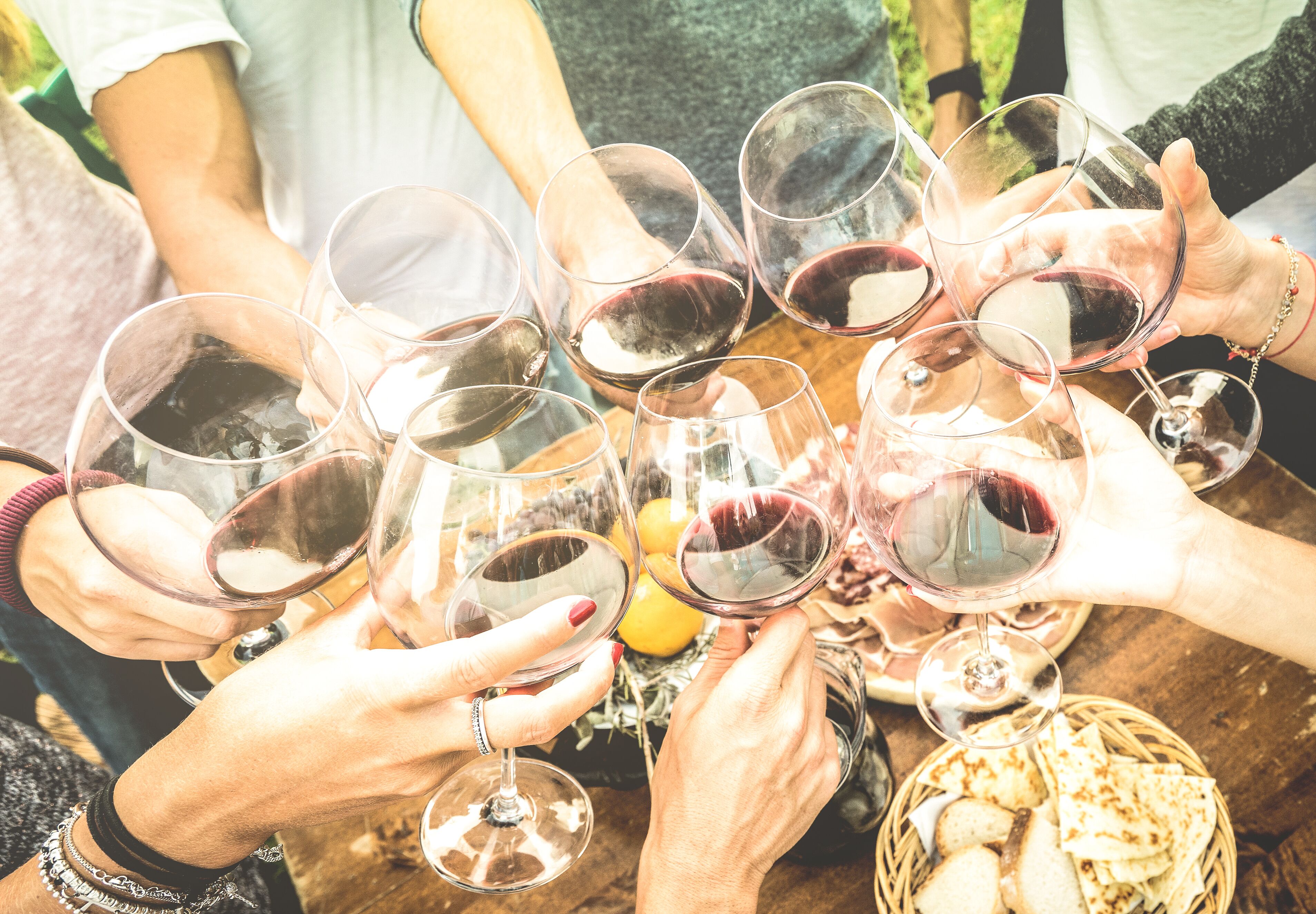 A group of people toasting with wine glasses around a table with bread and a basket.