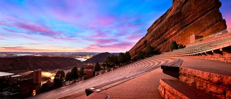 A large outdoor amphitheater with tiered seating, a stage, and a scenic backdrop of mountains and a sunset sky.