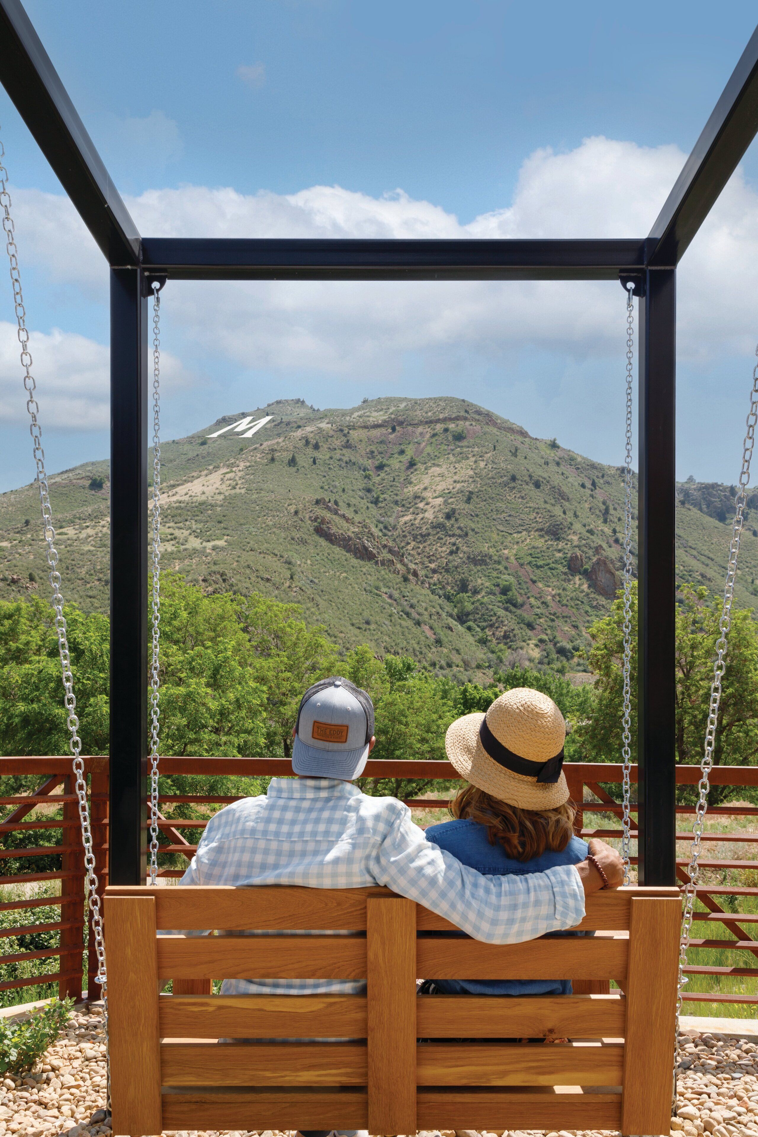 A wooden swing bench with metal chains, overlooking a mountainous landscape with a clear sky.