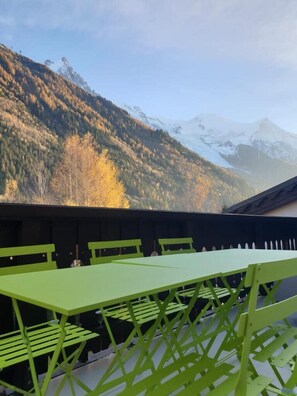 Un comedor con mesas y sillas verdes, con vistas a un paisaje montañoso de follaje otoñal y picos nevados.