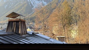 A view through a window of a building with a metal roof, a wooden structure on the roof, and a mountainous landscape in the background. - In the Heart of Chamonix duplex view Mont-Blanc (Chamonix-Mont-Blanc)