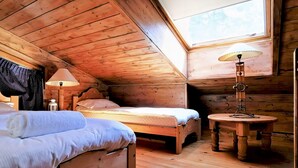 A cozy attic bedroom with wooden walls and a sloped ceiling, featuring two beds, a small round table, and a lamp. - In the Heart of Chamonix duplex view Mont-Blanc (Chamonix-Mont-Blanc)