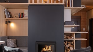 Ein modernes Wohnzimmer mit Kamin, Holzregalen und zwei schwarzen Sesseln.