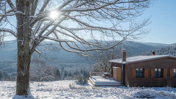 Eine Holzhütte mit einer Terrasse und Blick auf schneebedeckte Berge.