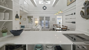 A modern kitchen with white cabinetry, a central island, and a dining area with a chandelier. - Renovated in Seaside, Sleeps 12! 3 Minutes to Beach! + 2 Adult Bikes! (Santa Rosa Beach)