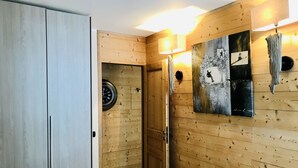 Una habitación con paneles de madera, una cama, un armario, una puerta que da a otra estancia y un reloj fijado a la pared.