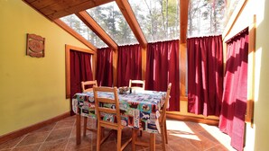 Ein Essbereich mit Tisch, bedeckt mit einer Patchwork-Tischdecke, Holzsesseln und roten Vorhängen.