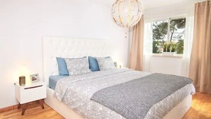 Ein Schlafzimmer mit einem großen Bett, einem Nachttisch, einer Pendelleuchte und einem Fenster mit Vorhängen.