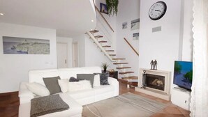 Ein modernes Wohnzimmer mit einem weißen Sofa, einem Kamin, einer Treppe und einem Fernseher.