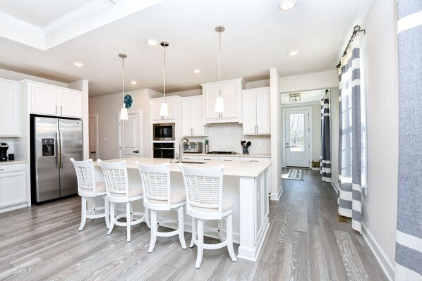 A modern kitchen with white cabinetry, stainless steel appliances, and a central island with bar stools.