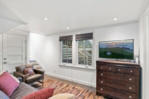 A living room with a sofa, a TV, a staircase, and a view of a golf course.