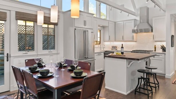 Une cuisine spacieuse avec des meubles blancs, un grand îlot central et des luminaires suspendus.