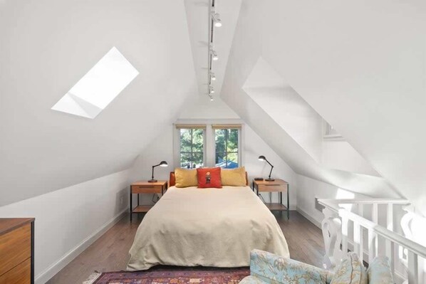 A bedroom with a sloped ceiling, a bed with pillows, bedside tables, and a window.