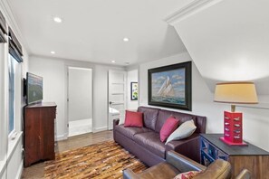 A living room with a brown leather sofa, a wooden coffee table, a patterned rug, a framed painting, and a red lamp. - Carmel's Wy Knot: Beautiful remodel in Carmel-by-the-Sea! (Carmel)