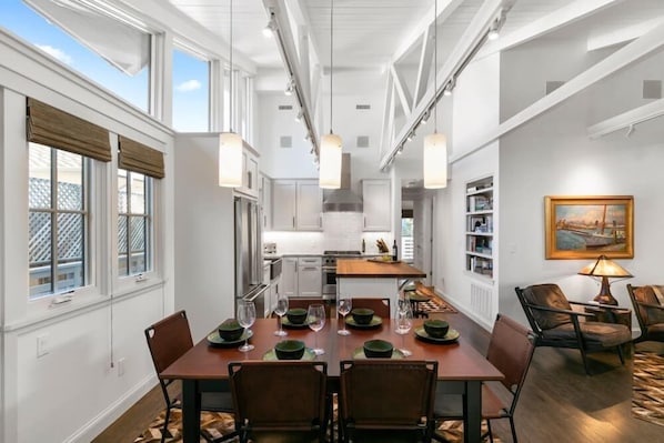 A dining area with a table set for four, a kitchen in the background, and a bookshelf with books. - Carmel's Wy Knot: Beautiful remodel in Carmel-by-the-Sea! (Carmel)