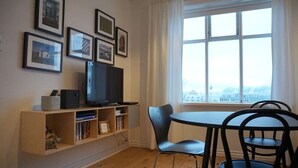 Une pièce avec un téléviseur posé sur une étagère en bois, une table avec des chaises et une fenêtre donnant sur un paysage.