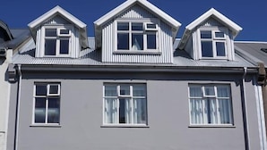 Un immeuble à plusieurs étages, doté d’une façade grise, de cadres de fenêtres blancs et d’une porte rouge.