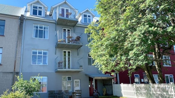 Un immeuble résidentiel à plusieurs étages, doté de balcons, d’un petit jardin et d’une clôture blanche en bois.