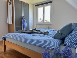 A bedroom with a bed, a window, and a hanging garment rack. - Wattkante Burhave, Apartment Hans & Grete (upper floor): 62 sqm, near the beach (Butjadingen)