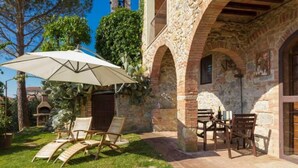 A stone building with a patio area featuring a table and chairs, a large umbrella, and a wooden chair. - Giovanna apartment on two levels overlooking the swimming pool (Castel San Gimignano)