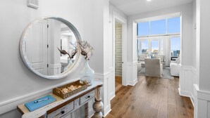 A hallway with a large mirror, a vase with dried branches, and a wicker basket on a wooden console. - Gulf-Front Retreat with Panoramic Views (Watersound)