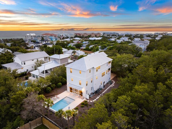 A residential area with houses, a swimming pool, and a view of the ocean at sunset.