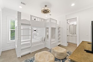 A bedroom with a bunk bed, built-in shelving, a large mirror, and a wooden table.