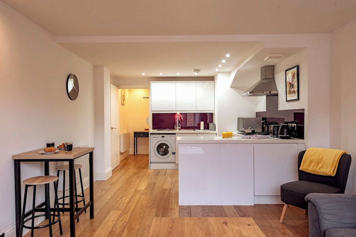 Cocina compacta con isla central, lavadora y zona de comedor con taburetes.