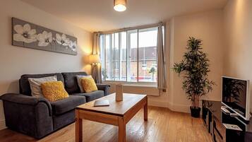 Una sala de estar con un sofá, una mesa de centro, una lámpara, un mueble para televisión y una ventana con cortinas.