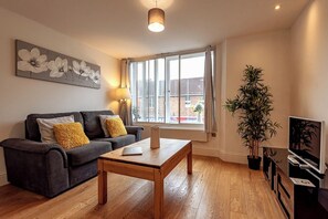 A living room with a sofa, a coffee table, a lamp, a TV stand, and a window with curtains.