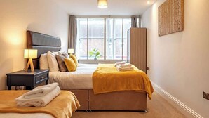 Ein Hotelzimmer mit Bett, Nachttisch, Fenster mit Vorhängen und Wandgemälde.