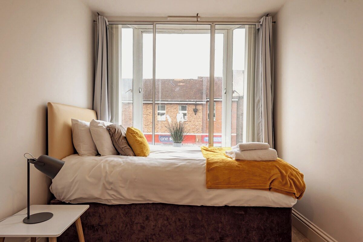 A bedroom with a bed, a bedside table, a lamp, and a window with curtains.