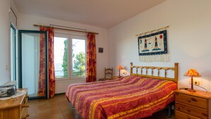 Une chambre à coucher avec un lit, une commode en bois, une table de chevet avec une lampe, une chaise et une fenêtre avec des rideaux.