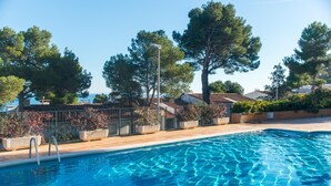 Une piscine à l’eau d’un bleu limpide, entourée d’arbres et de plantes en pot.