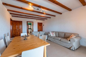 A dining area with a wooden table and chairs, a beige sofa, and wooden beams on the ceiling.