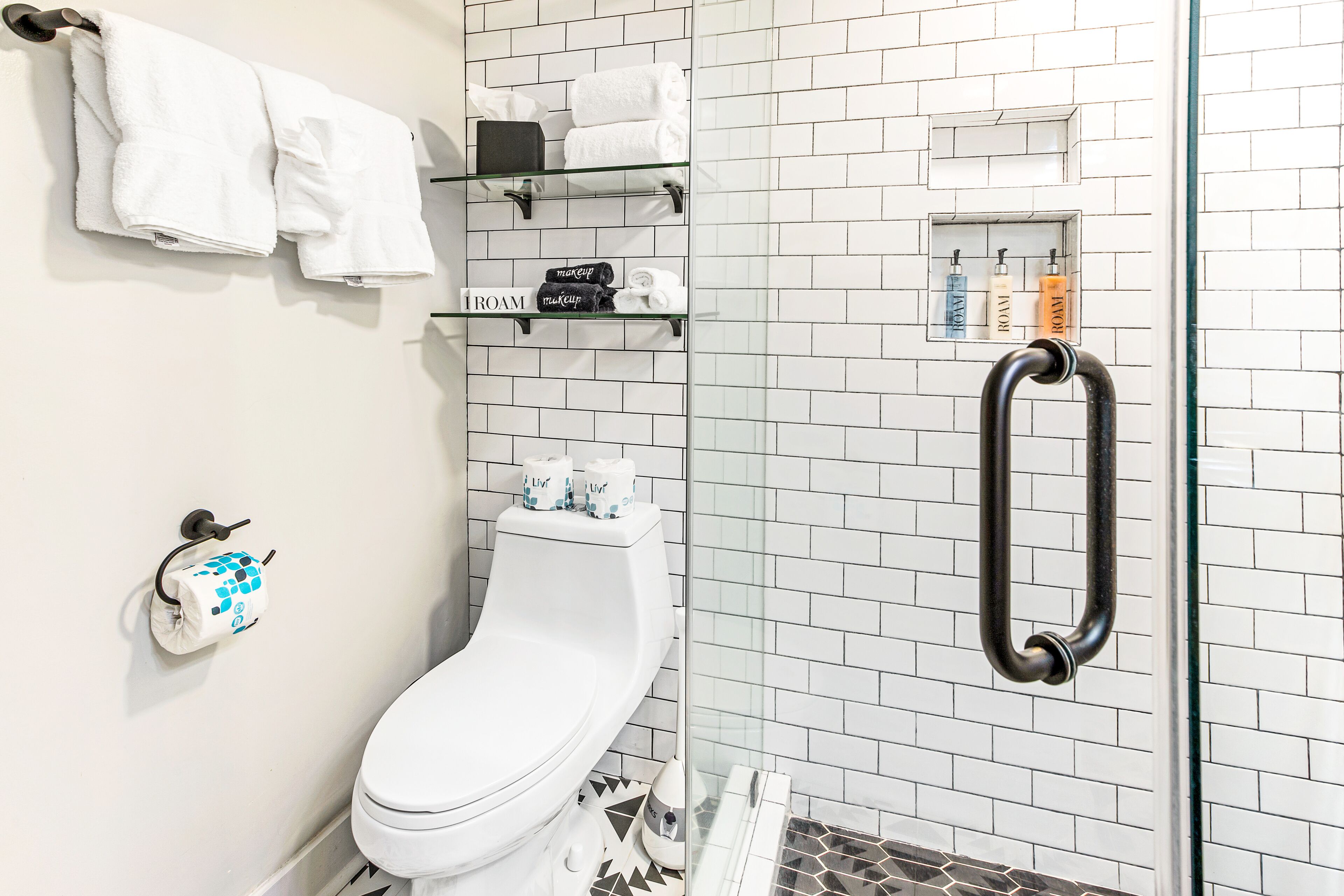 A modern bathroom with a toilet, a glass shower enclosure, and a handrail.