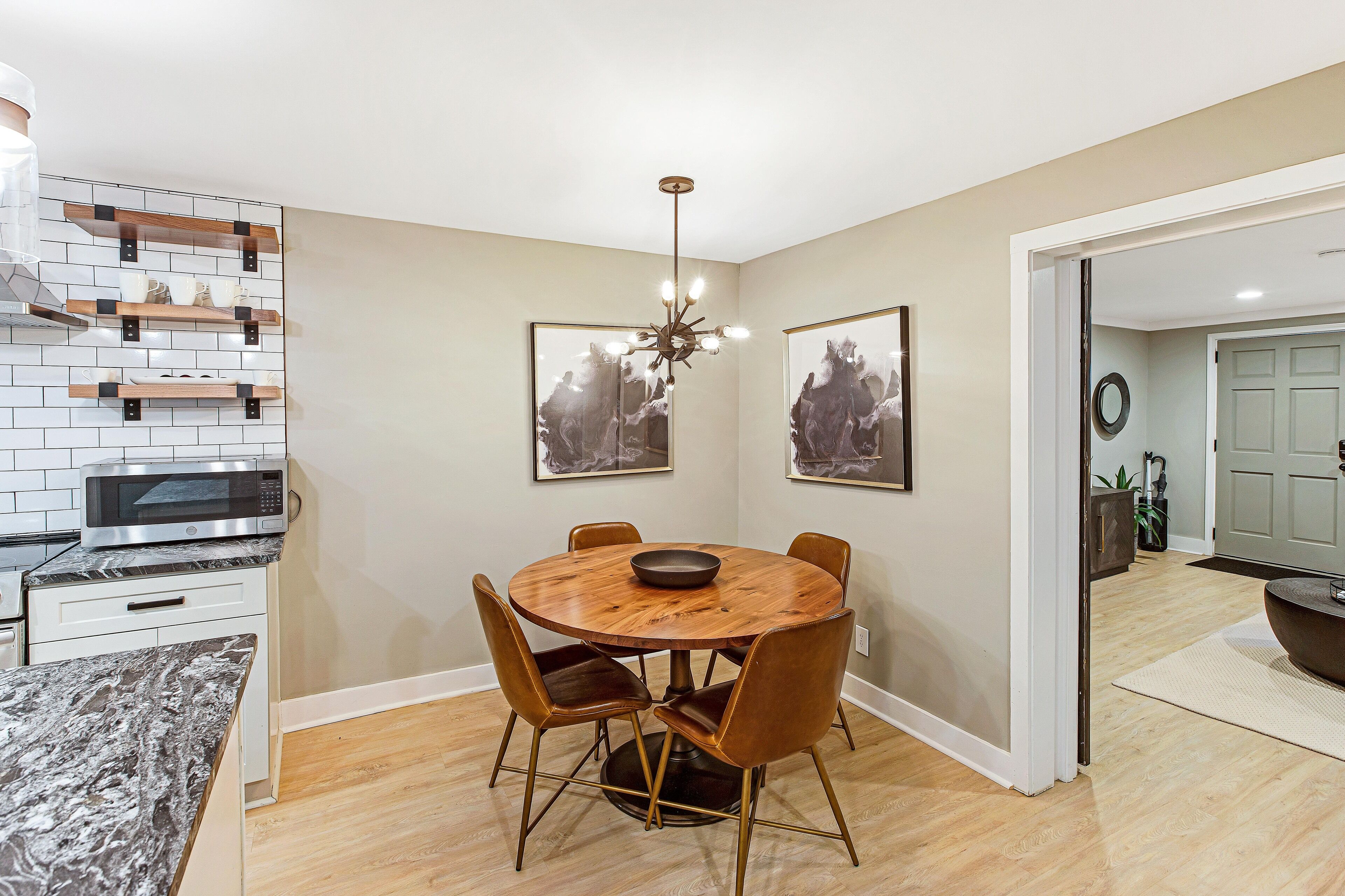 A dining area with a round wooden table, six chairs, a chandelier, and artwork on the walls.