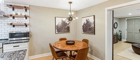 A dining area with a round wooden table, six chairs, a chandelier, and artwork on the walls.