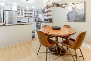 A modern kitchen with a central island, stainless steel appliances, and a dining area with a round table and leather chairs. - Modern Garden Apartment with High-end Amenities on Jones by Lucky Savannah (Savannah)