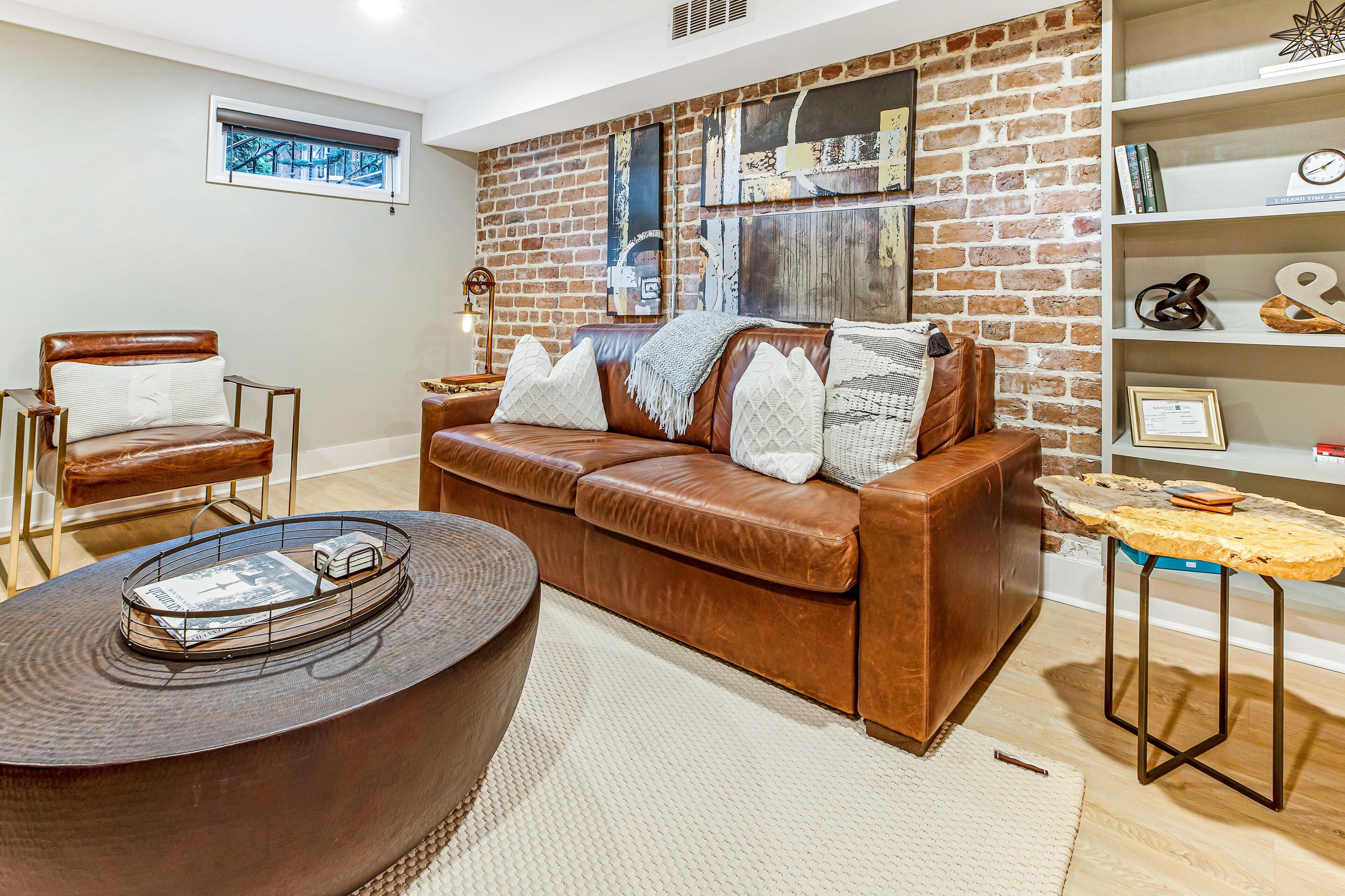 A living room with a brick wall, a brown leather sofa, a round coffee table, and a bookshelf.