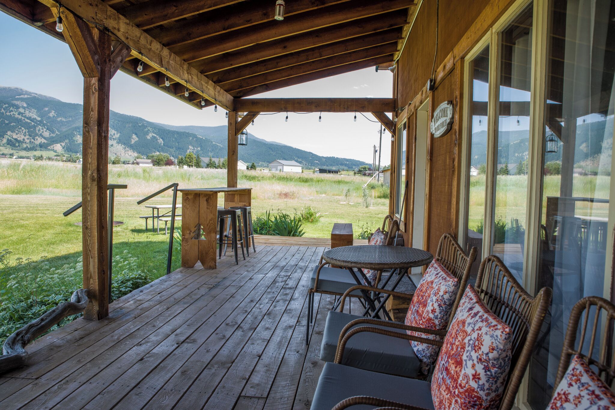 A wooden deck with outdoor seating, a table, and a view of a grassy field and mountains.