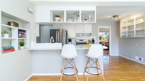 Une cuisine moderne avec des meubles blancs, un réfrigérateur en acier inoxydable et deux tabourets de bar blancs.