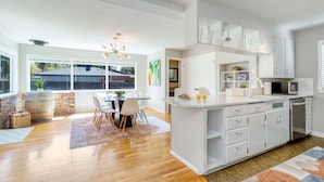 Une cuisine moderne avec des meubles blancs, un îlot central et un coin repas comprenant une table et des chaises en verre.