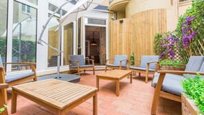 An outdoor patio with wooden furniture, including tables and chairs, and a wooden fence with climbing plants. - Cosmopolitan Boutique Rambla (Barcelona)