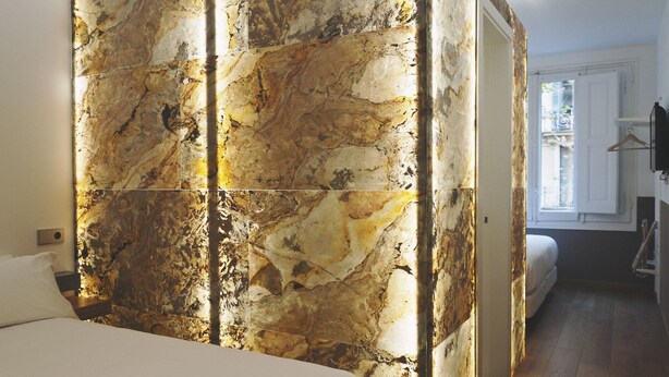 A bedroom with a large bed, a marble wall, and a view of a cityscape through a window. - Cosmopolitan Boutique Rambla (Barcelona)