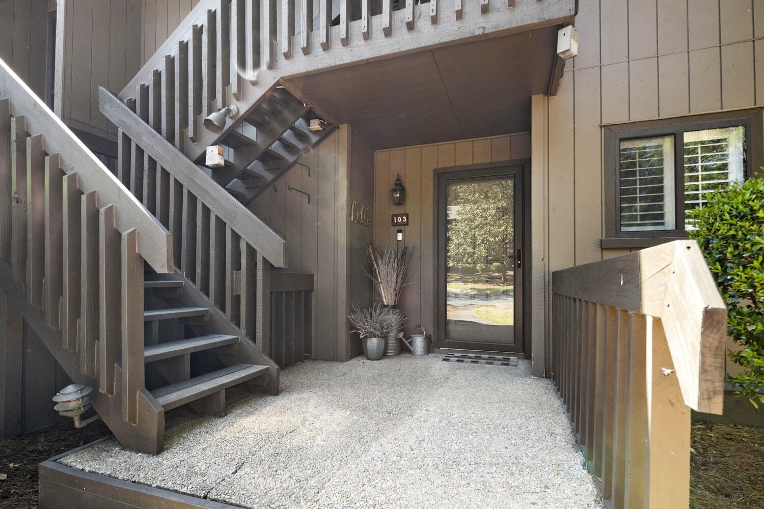 A wooden staircase leading to a door with a number plate, a small garden area with gravel, and a metal gate.
