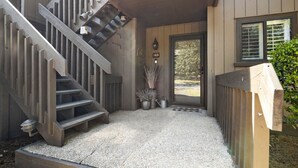 A wooden staircase leading to a door with a number plate, a small garden area with gravel, and a metal gate.