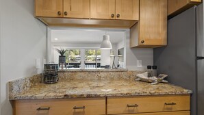 A kitchen with wooden cabinets, granite countertops, and a view of an outdoor patio.