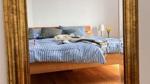 Ein Schlafzimmer mit einem hölzernen Bett, gestreifter Bettwäsche, einer Nachttischlampe und einer Vase mit Blumen.